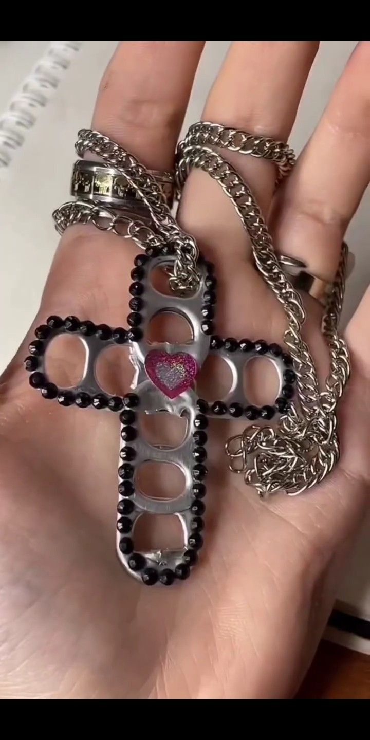 a hand holding a cross shaped pendant with chains on it's thumb and the word love is in the middle