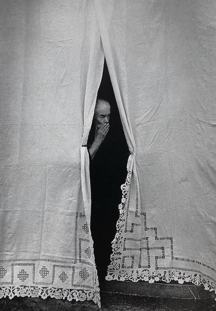 an old black and white photo of a man peeking out from behind curtains