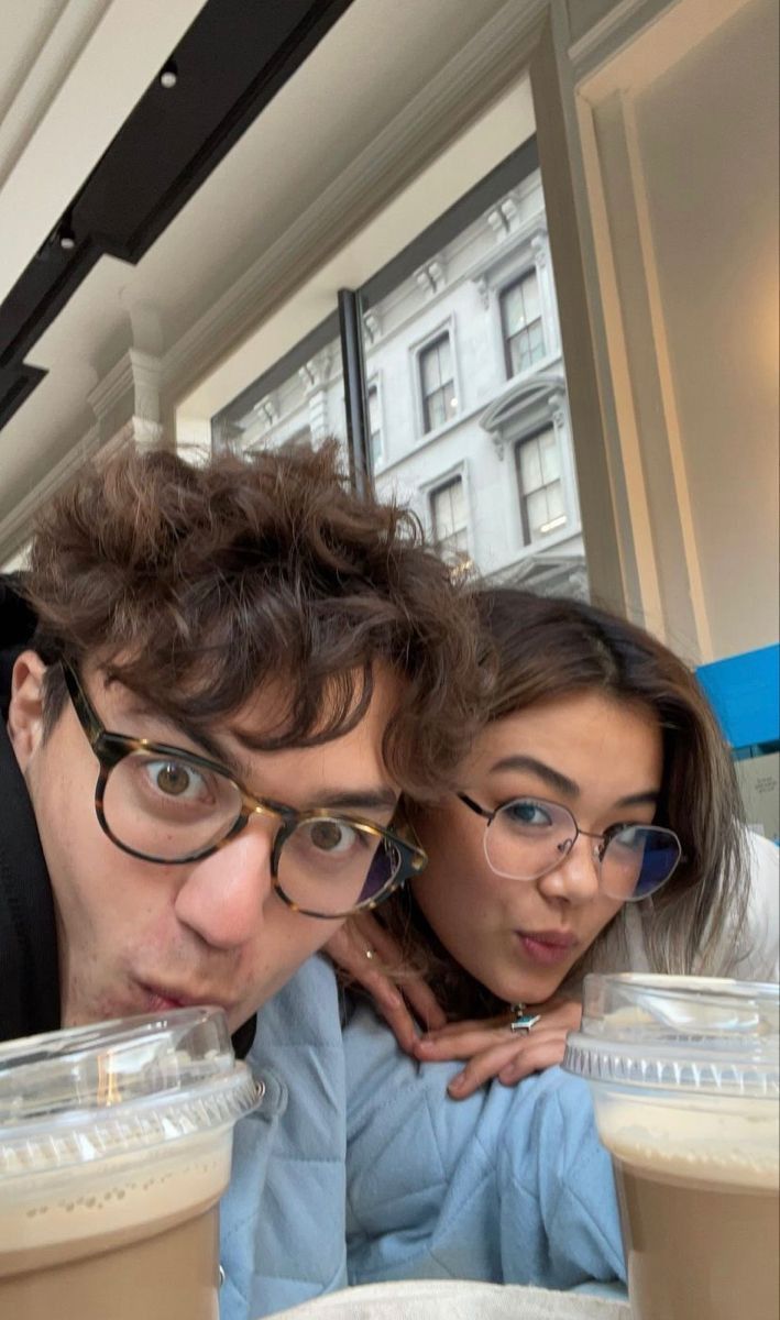 two people are posing for the camera with drinks in front of their faces and looking at the camera