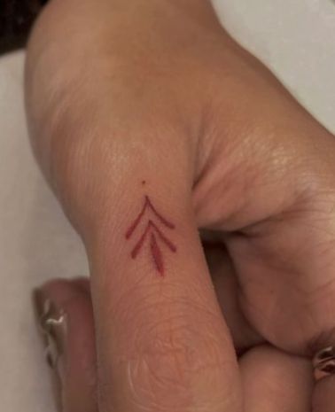 a woman's left hand with a red arrow tattoo on it