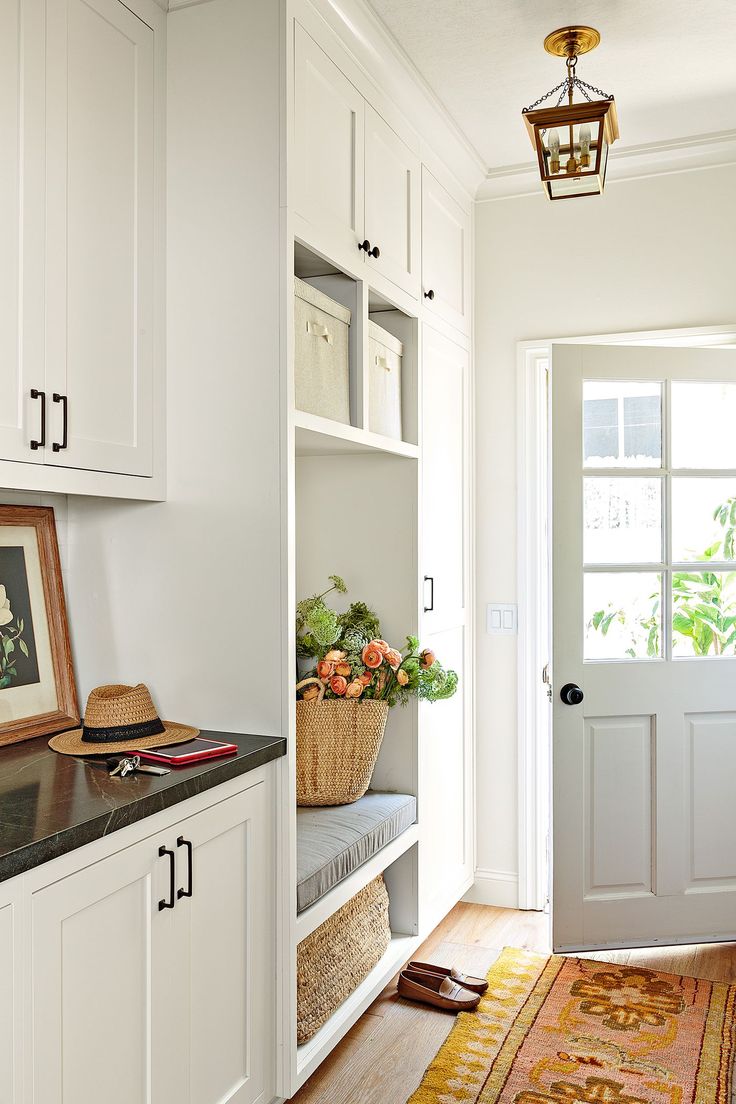 an entryway with white cabinets and baskets on the shelf, next to a door