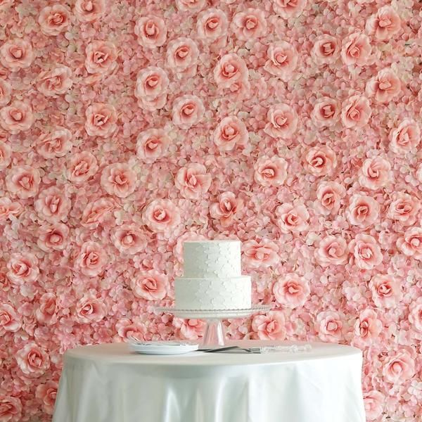 a white cake sitting on top of a table in front of a flower covered wall