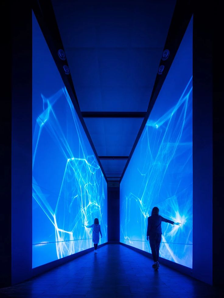 two people are walking in front of blue lights and projected images on the wall behind them