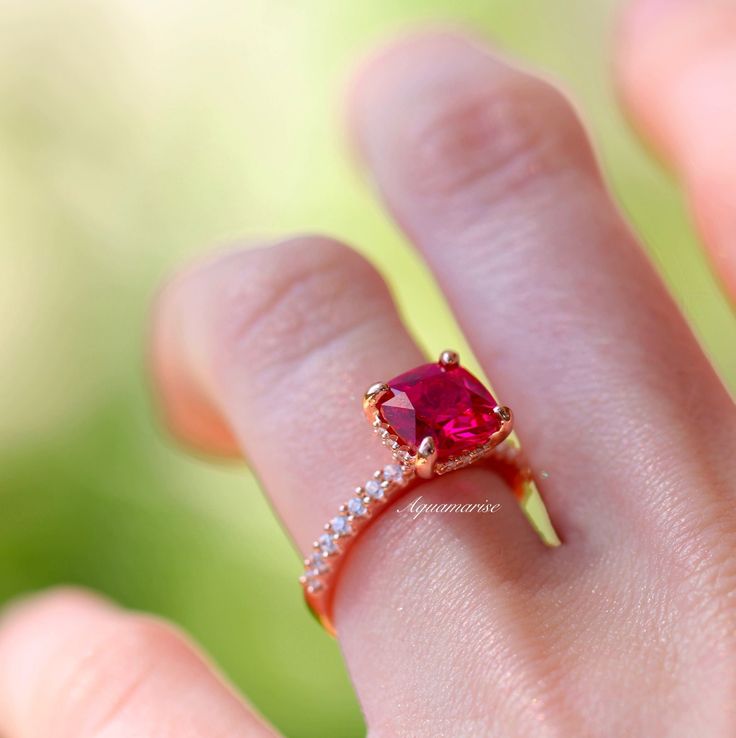 a close up of a person's hand holding a ring with a red stone