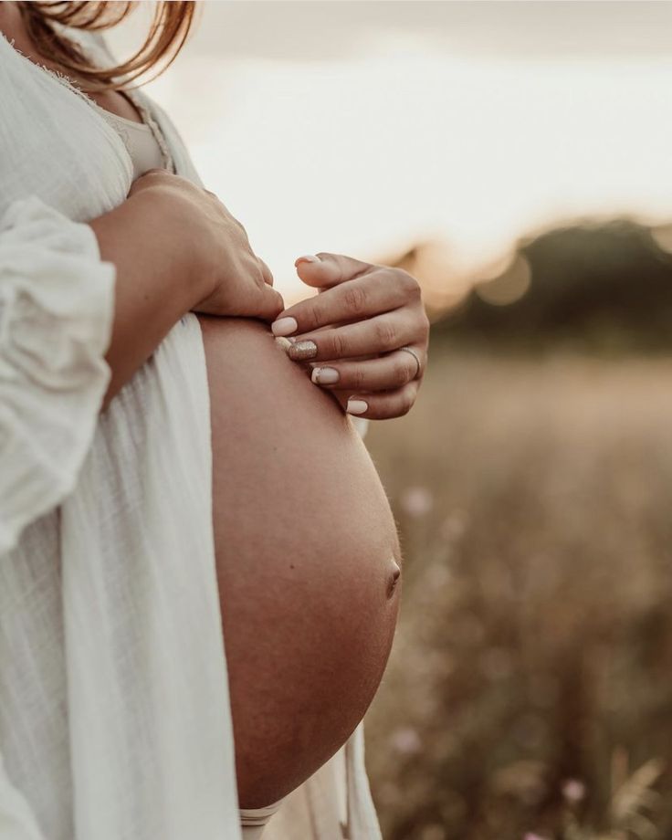 a pregnant woman holding her belly in the middle of a field