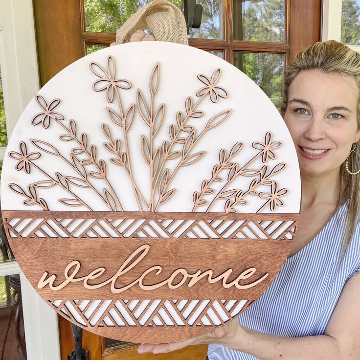 a woman holding up a welcome sign in front of a door with flowers on it