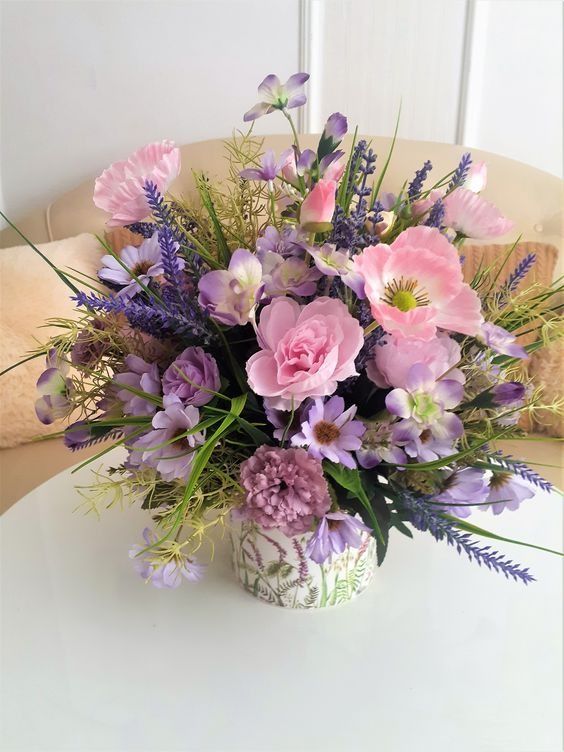 a white vase filled with purple flowers on top of a table next to a pillow