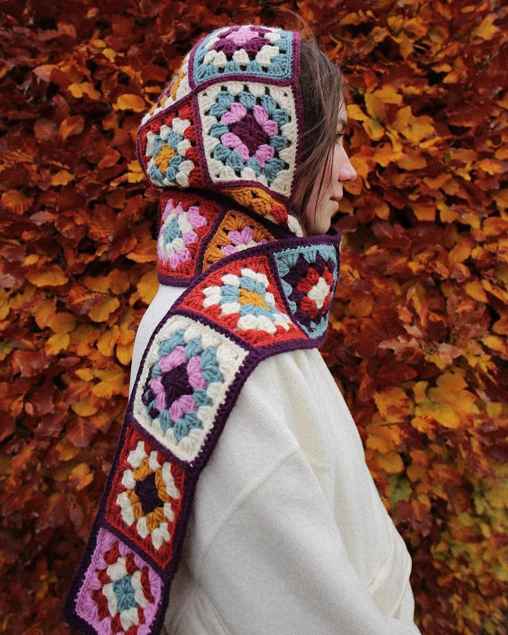 a woman is wearing a crocheted scarf and hat in front of some leaves