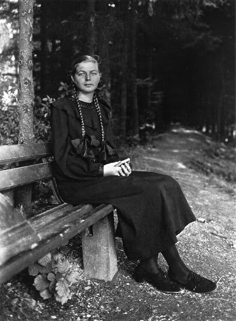 an old photo of a woman sitting on a wooden bench in the middle of a forest