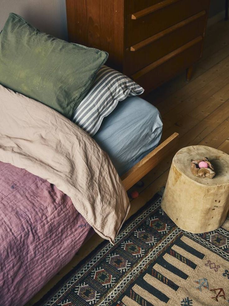 a bed with pillows and blankets on top of it next to a wooden dresser in a bedroom