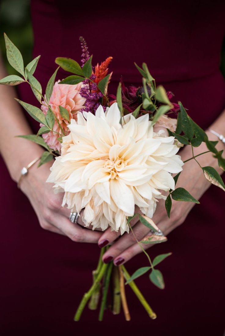 a woman in a maroon dress holding a bouquet of white and pink flowers with greenery