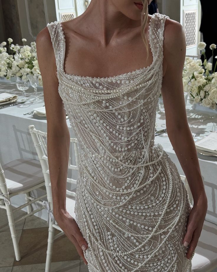 a woman standing in front of a table wearing a dress with beading on it