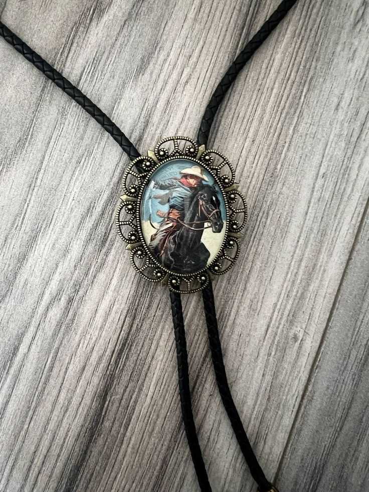 Our handmade western bolo tie has a vintage cowboy with a glass coating. PERFECT for a country men’s bolo tie, wedding sting tie, necktie for groomsmen, or any special person in your life. This bolo tie for men (and women!) has a metal clamp which makes it easy to adjust. *Makes a Great Gift*Pendant Size: 1.5 in x 1.25 inCord in Black Genuine Leather: 39in Riding Black Horse, Bolo Tie Wedding, Western Bolo Tie, Gold Bow Tie, Yellow Bow Tie, Purple Bow Tie, Plaid Bow Tie, Bowtie And Suspenders, Leather Suspenders