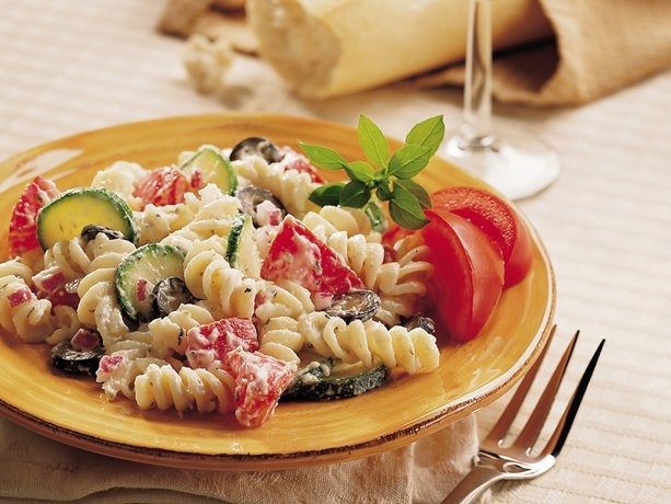 a yellow plate topped with pasta salad next to a fork and glass of red wine