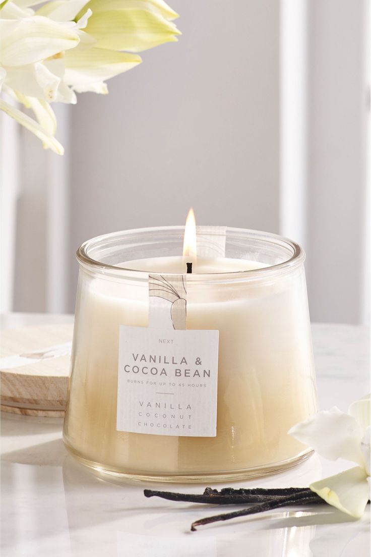 vanilla and cocoa bean candle sitting on top of a table next to some white flowers