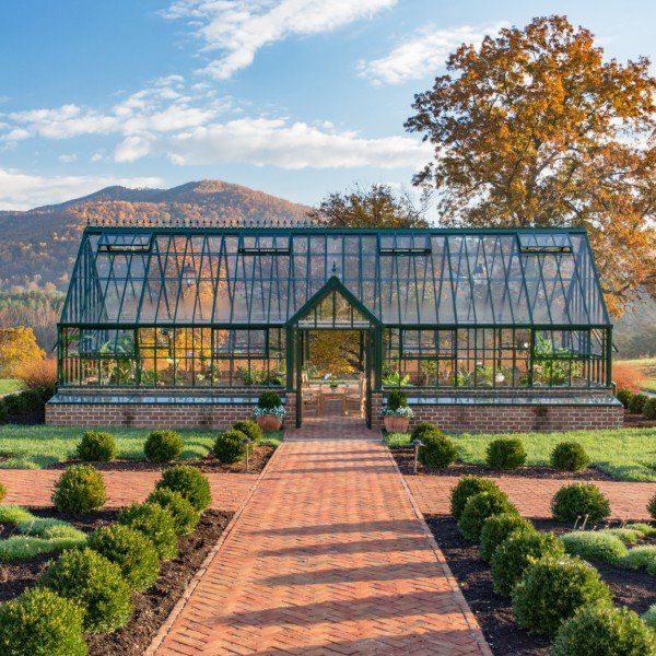 a glass house in the middle of a garden with green hedges and bushes around it