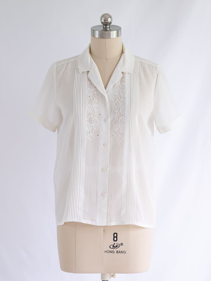 Step into a world of ethereal beauty with our Sugar Cream Vintage polyester blouse. Its collared neck, adorned with delicate scallop detailing and front buttons, evokes timeless charm. The half sleeves and intricate pintex detailing, accentuated by whimsical floral embroidery, create a captivating look that's both unique and exquisite. Care: Cool machine wash. Dry at a lower heat and press with a medium iron.  Condition: Embrace the distinctive charm of this upcycled treasure, where imperfection Elegant White Blouse With Placket Detail, Elegant White Blouse With Placket, Elegant Tops With Peter Pan Collar And Buttons, Elegant Fitted Blouse With Scalloped Edges, Elegant Blouse With Scalloped Edges, Classic Wedding Blouse With Buttons, White Feminine Blouse With Collared Neckline, Feminine White Blouse With Collared Neckline, Elegant Summer Tops With Peter Pan Collar