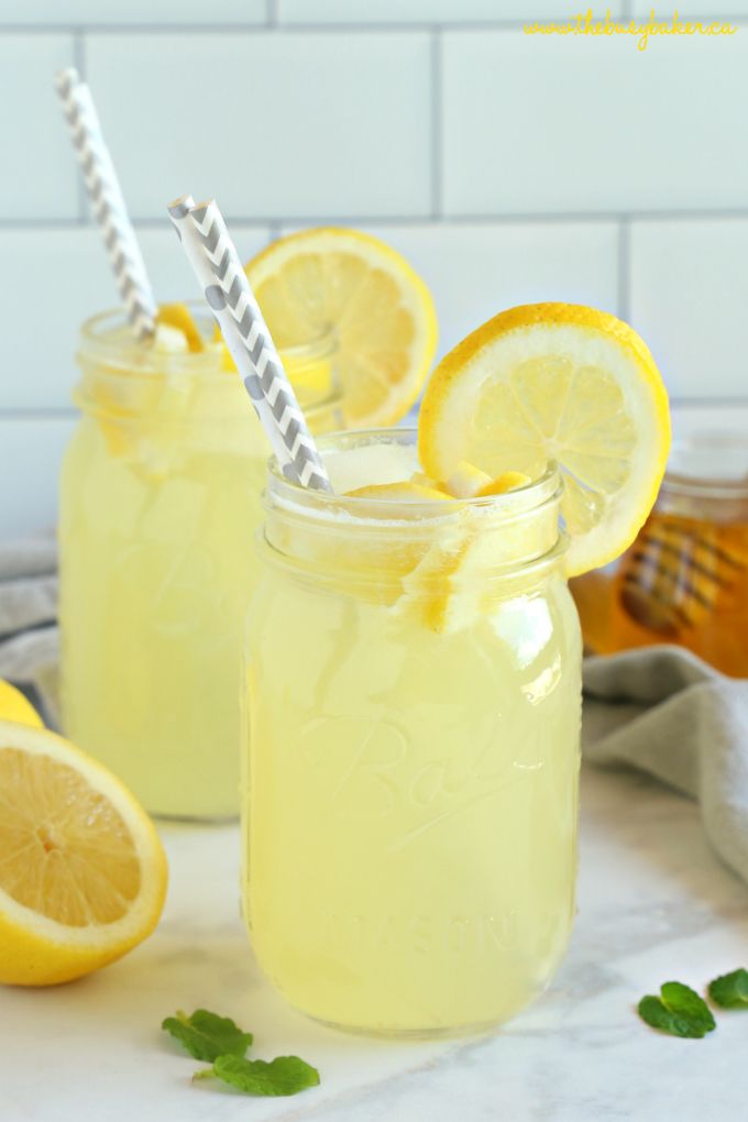 lemonade in mason jars with straws and lemons around them on a table