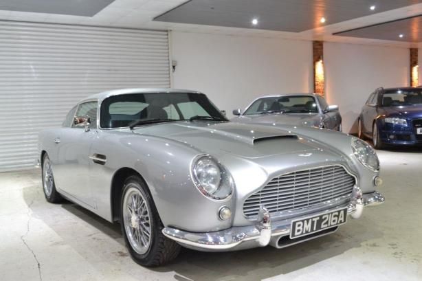 two cars are parked in a garage with one is silver and the other is blue