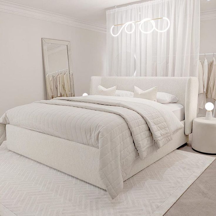 a white bedroom with a bed, mirror and lamps on the side of the room