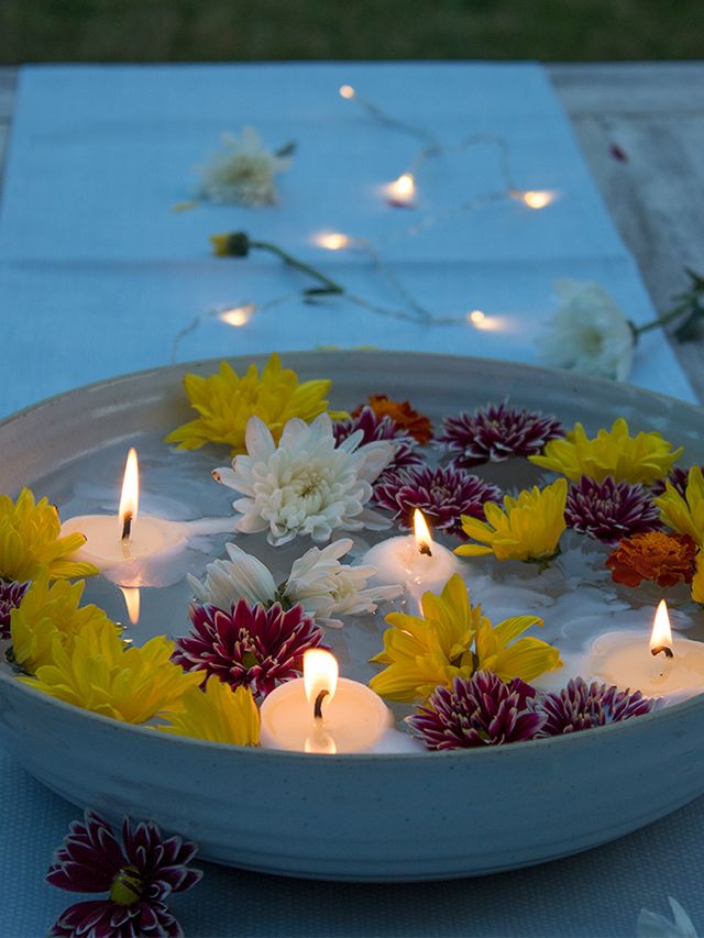 candles are floating in a bowl filled with water and flowers on a blue table cloth