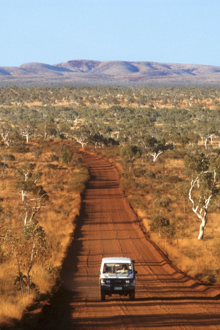 a van is driving down a dirt road in the middle of an outback area