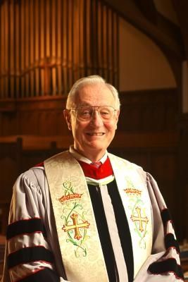 an older man wearing a priest's robe in front of a pipe organ