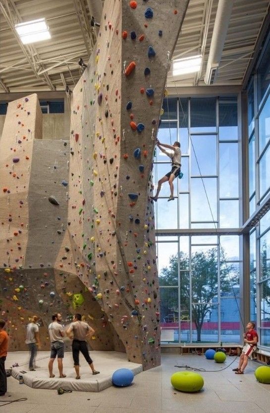 several people are climbing up and down the walls in an indoor climbing area with large windows