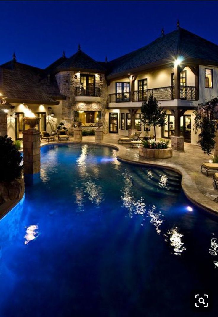 a large house with a swimming pool in the middle of it at night, lit up by lights