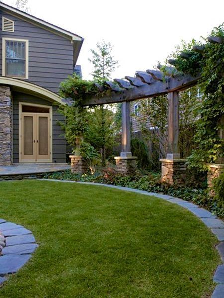 an outdoor patio with stone walkway and pergolated area in the foreground, surrounded by green grass