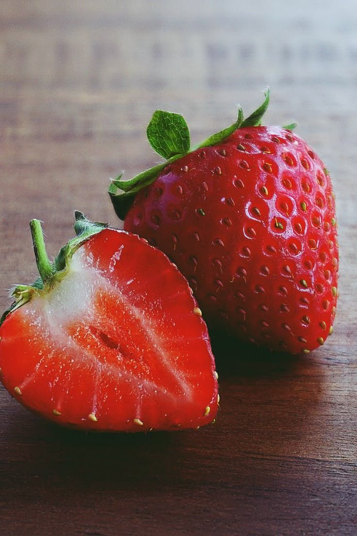 two strawberries sitting on top of a wooden table next to each other, one has a bite taken out of it