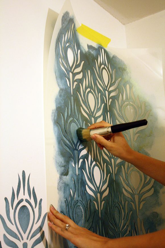 a woman is painting a wall with blue and white designs on the paper, while holding a paintbrush in her hand