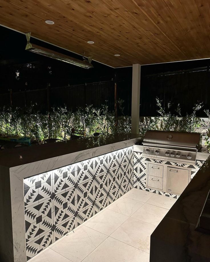 an outdoor kitchen is lit up at night with lights shining on the counter and grill