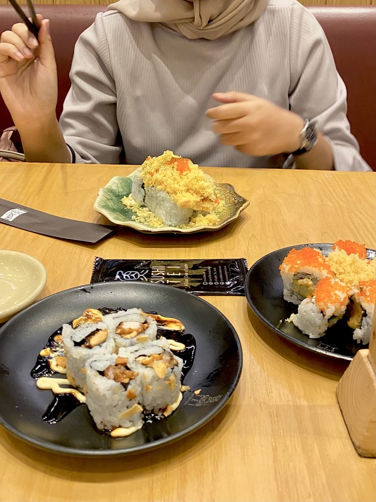 a woman sitting at a table with two plates of sushi and chopsticks in front of her