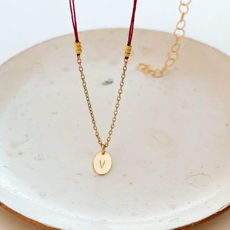 A very delicate necklace featuring double red thread strands, tiny golden nuggets on the sides, an oval simple shape pendant with a little piece of 14K gold fill chain on the bottom.The pendant is custom stamped with the letter of your choice. Please, type the letter you want to be stamped on your pendant at check-out!∙ Only 1 letter permitted.∙ We use only capital letters.In many cultures, the color red is traditionally used as a symbol of protection, good luck, or blessing. In my native Argent Dainty Oval Pendant Chain Necklace As Gift, Delicate Chain Necklace With Oval Pendant For Gift, Gift Oval Pendant Chain Necklace With Adjustable Chain, Oval Pendant Necklace With Delicate Chain As Gift, Delicate Oval Pendant Chain Necklace As Gift, Adjustable Chain Necklace With Oval Pendant, Gold Plated Chain Necklace With Oval Pendant, Gift Cable Chain Necklace With Oval Pendant, Red Gold Chain Necklace For Gifting