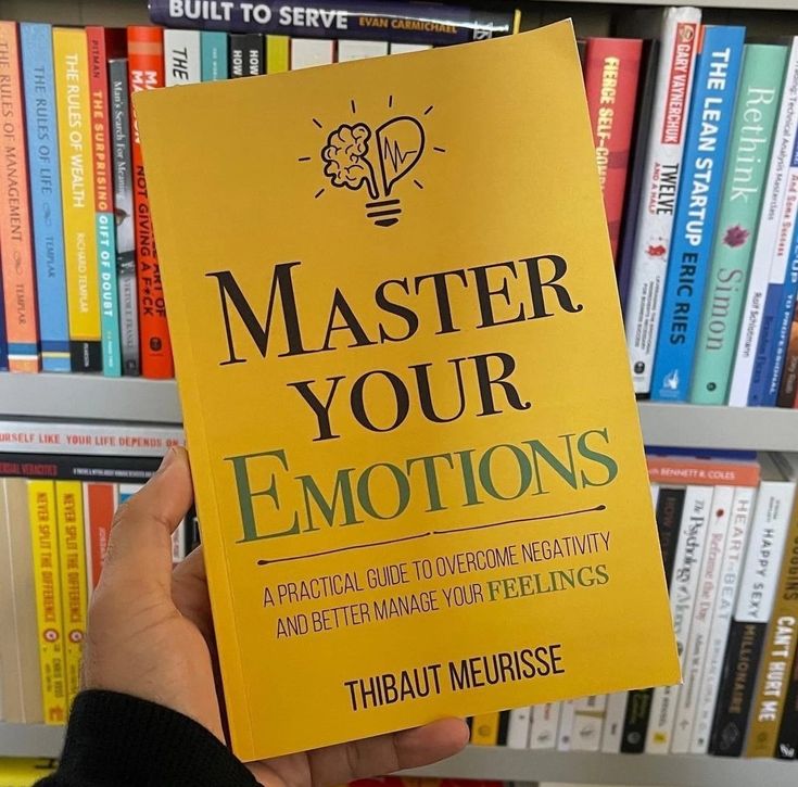 a person holding up a yellow book in front of a bookshelf full of books