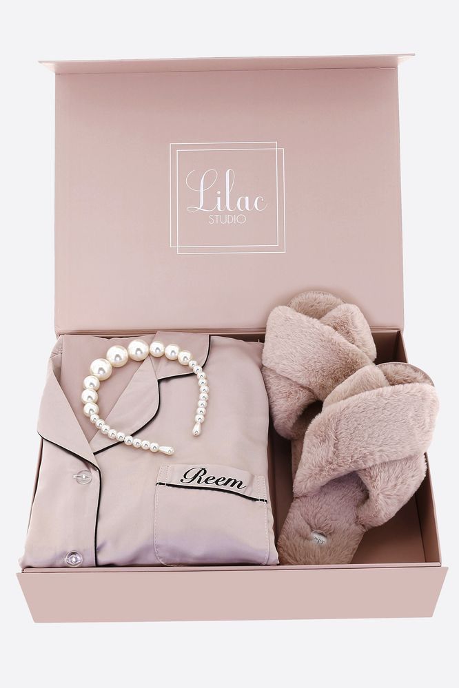 an open box containing a pink shirt, white pearls and a pair of slippers