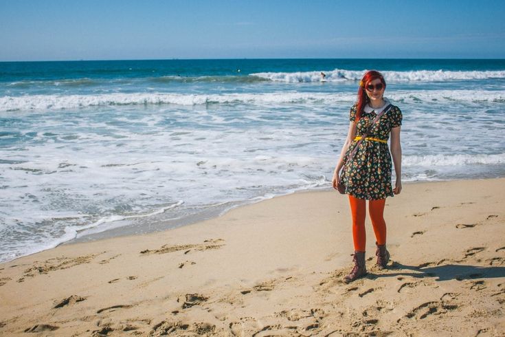 a woman standing on top of a sandy beach next to the ocean