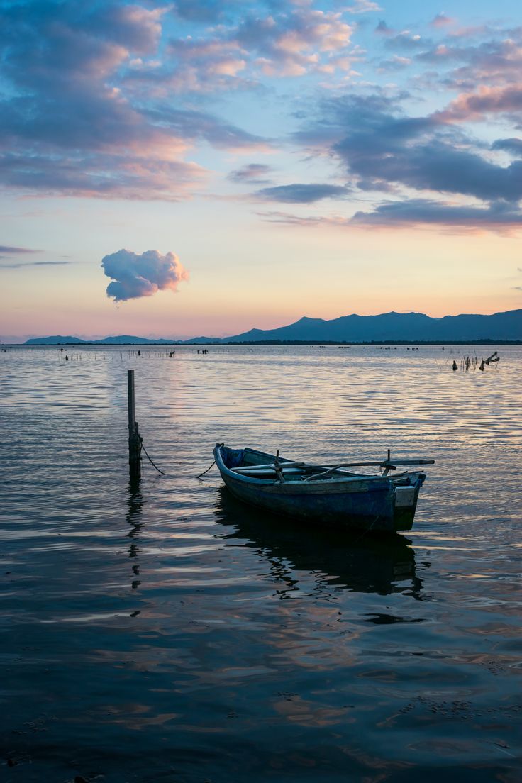 a small boat sitting on top of a body of water under a cloudy blue sky