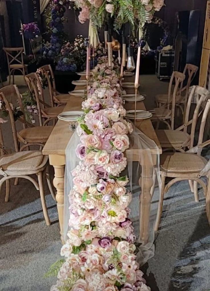 a long table with flowers on it and chairs around the table in front of it