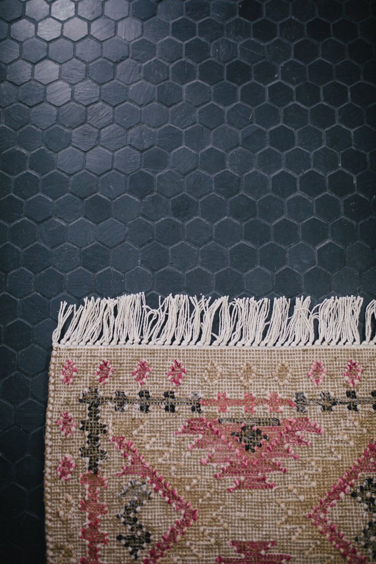 the rug is laying on the floor in front of the black tiled wall with hexagonal tiles