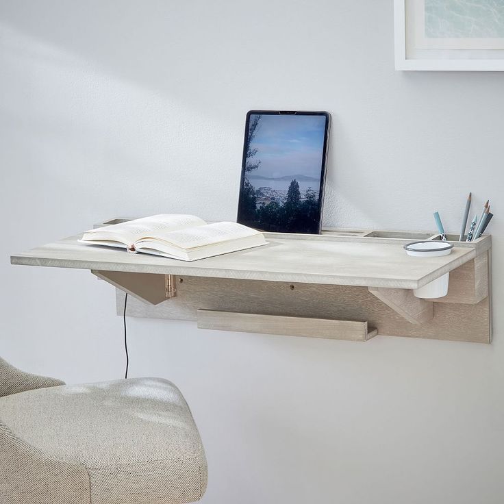 a laptop computer sitting on top of a wooden desk next to a white chair and wall