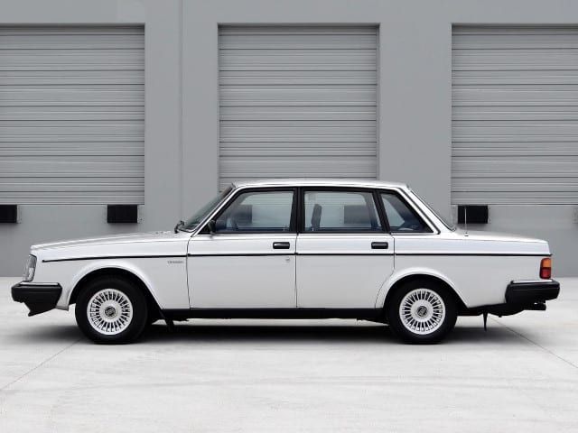 an old white car is parked in front of some garage doors with roller doors behind it