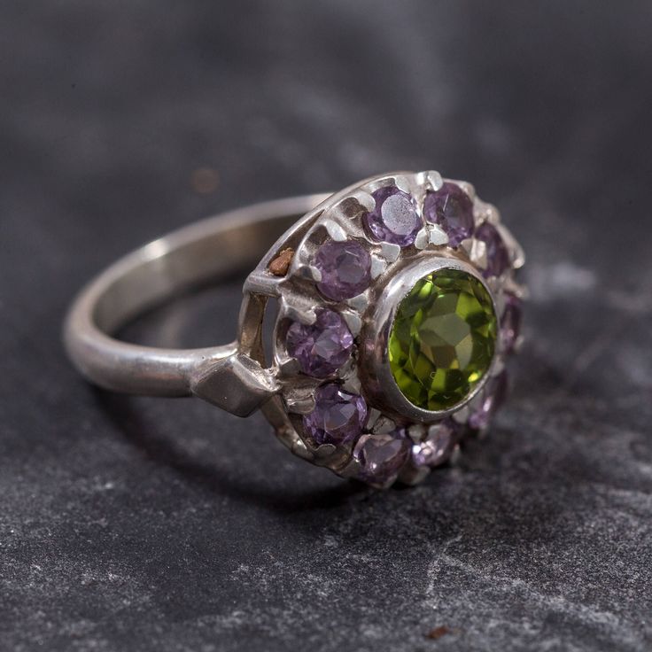 Peridot Ring set with Natural Peridot in a diamond cut & natural green color, at size 7mm together with Natural Amethyst at size 3mm each (2.3 Cts combined) from Brazil.Solid 925 Sterling Silver ☞ made to last.Click here for ☞ Matching PendantClick here for ☞ Matching EarringsClick here for ☞ Flower Collection Details:• Natural Peridot & Amethyst sourced from Brazil• Peridot: 7mm, 1.3 Cts, diamond cut• Amethyst: 3mm each, 1 Ct total, diamond cut• Dimensions: Band width ≈ 2.3mm, thickness ≈ 1.3mm Green Amethyst Multi-stone Jewelry, Green Multi-stone Amethyst Jewelry, Peridot Multi-stone Rings For May Birthstone, Green Amethyst Ring In Sterling Silver, Green Amethyst Ring Fine Jewelry, Green Sterling Silver Amethyst Ring For Wedding, Green Amethyst Promise Ring In Fine Jewelry Style, Green Amethyst Rings In Fine Jewelry Style, Round Peridot Gemstones With Accent Stones