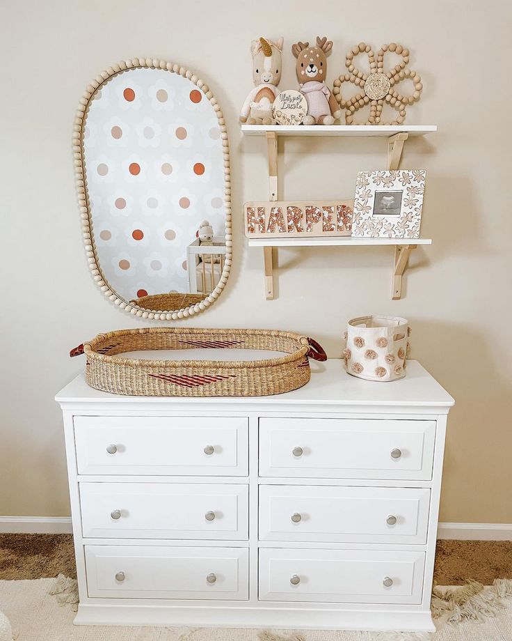 a white dresser topped with a baby's crib next to a wall mounted mirror