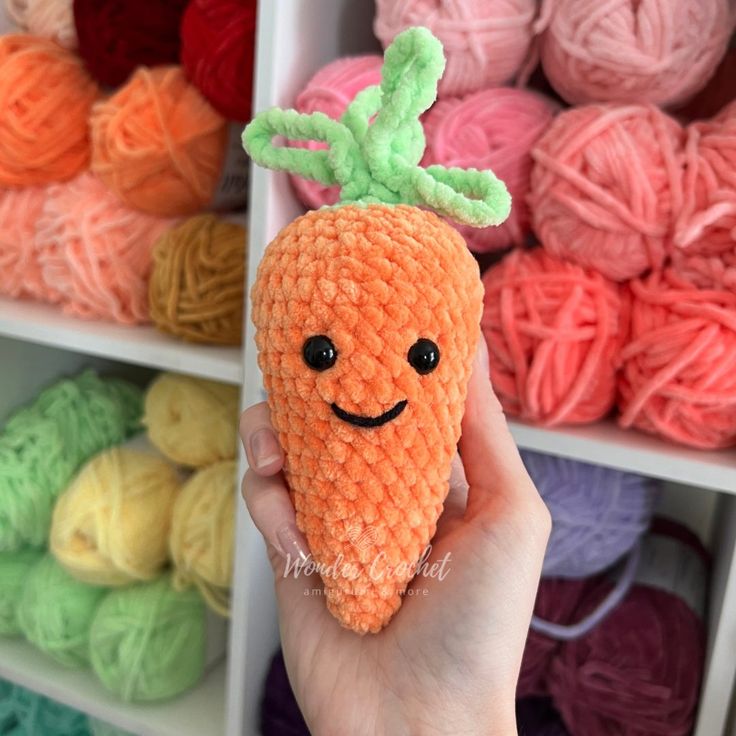 a hand holding up a knitted carrot with a smiling face on it's head