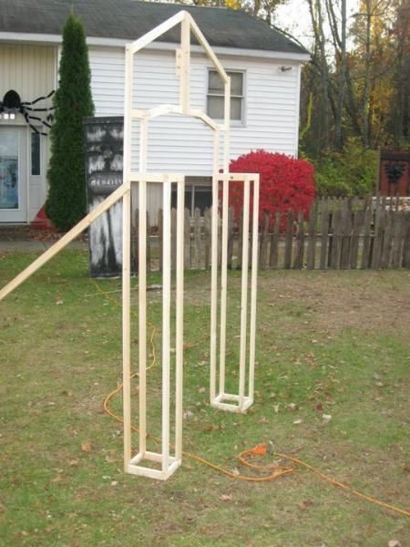 two white metal structures sitting in the grass near a house with a spider on it's back