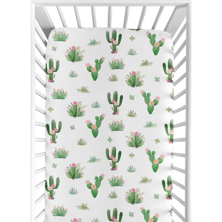 a crib bed with cactus and flowers on the sheet in white, next to it is