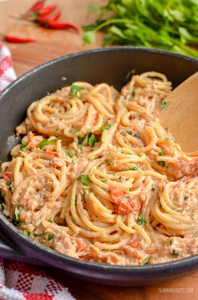 a skillet filled with pasta and sauce on top of a wooden table next to parsley