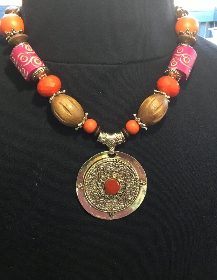 Necklace by Erica Lyons is 12 inches long and adorned with multiple materials; pendant, beads, spacers, chain, and lobster clasp.  Colors include; red, orange, brown, and gold.  Pendant is 2-3/8 inches in diameter with a red stone inlaid.  The necklace weighs 3.5 ounces. Red Stone, Orange Brown, Gold Pendant, Pendant Necklaces, Lobster Clasp, Favorite Jewelry, Necklace Etsy, Jewelry Necklace Pendant, Beauty Book